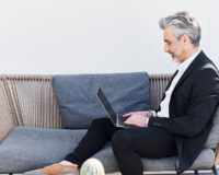 man sitting on couch typing on his laptop